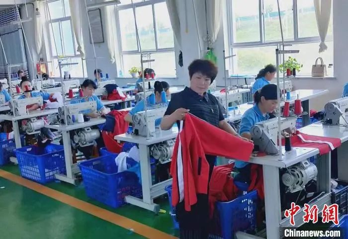 图为临夏县翠梦飞服装加工有限责任公司总经理唐小翠(中)在制衣工厂内检查衣服质量