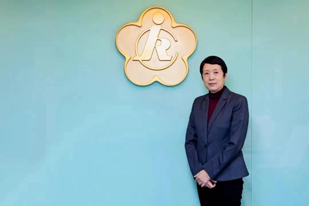 图为龙墨在中国残疾人福利基金会会徽前留影