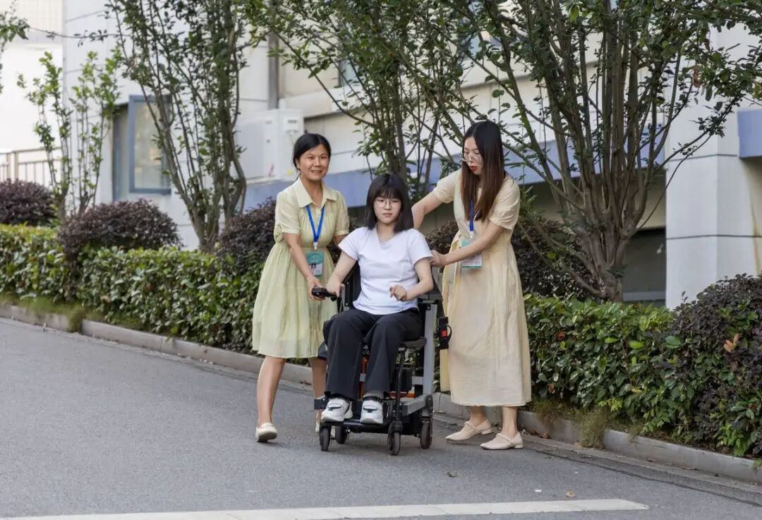 图为曹慧婷在妈妈张胜兰（左）和送考老师的帮助下，坐着轮椅“走”出考场